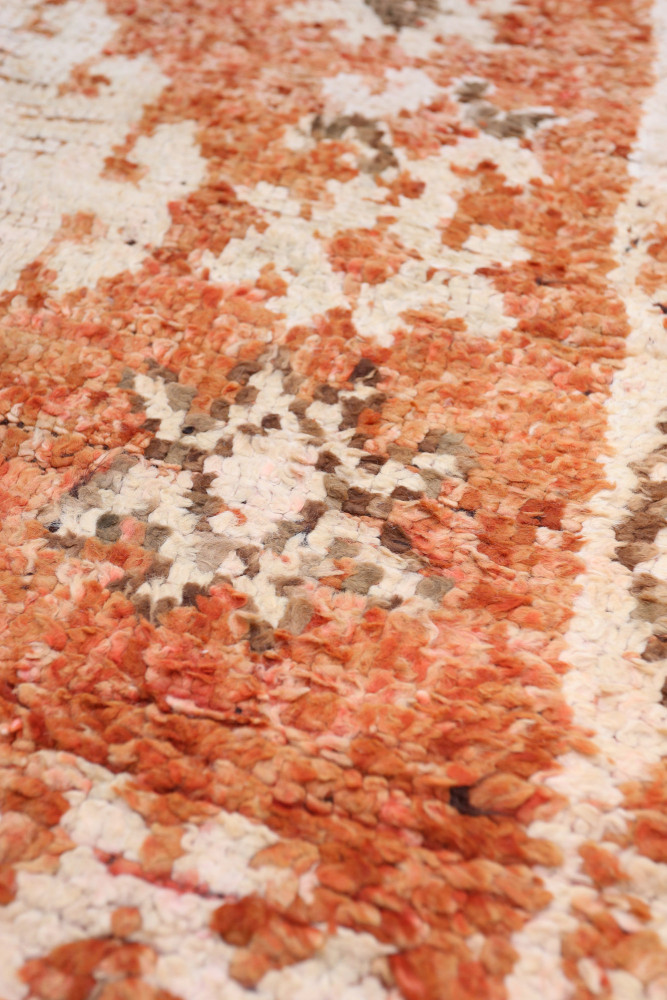 Tapis berbère aux motifs géométriques avec des nuances chaudes d\'orange, beige et marron.