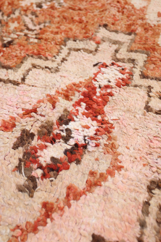 Tapis berbère aux motifs géométriques dans des teintes rose, rouge et beige, ajoutant une touche chaleureuse à votre intérieur.