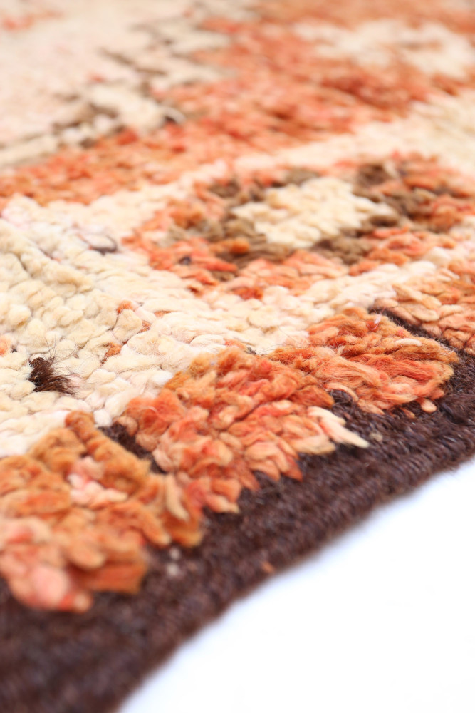Tapis berbère aux teintes chaudes d\'orange et beige avec des motifs géométriques texturés.