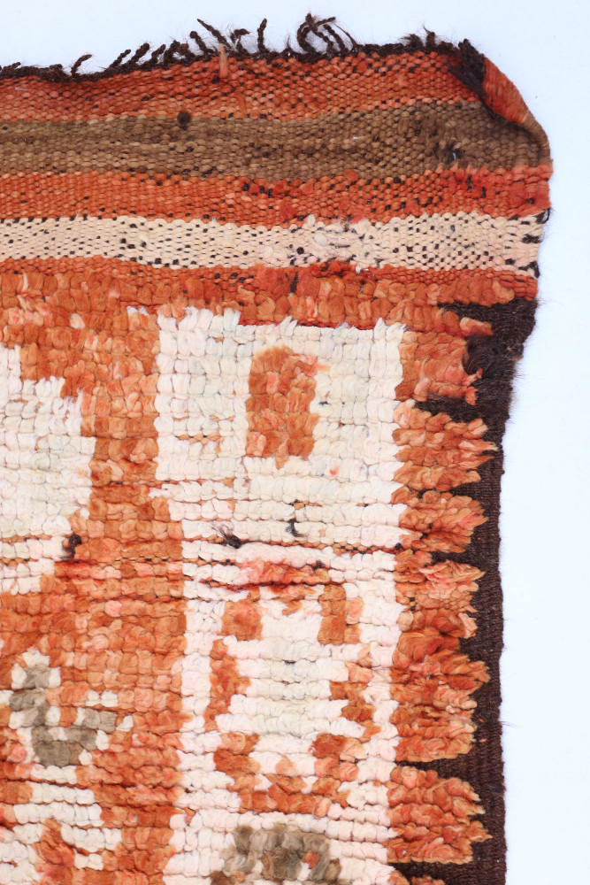 Tapis berbère en laine, motifs géométriques, couleurs chaudes comme l\'orange, le beige et le brun.