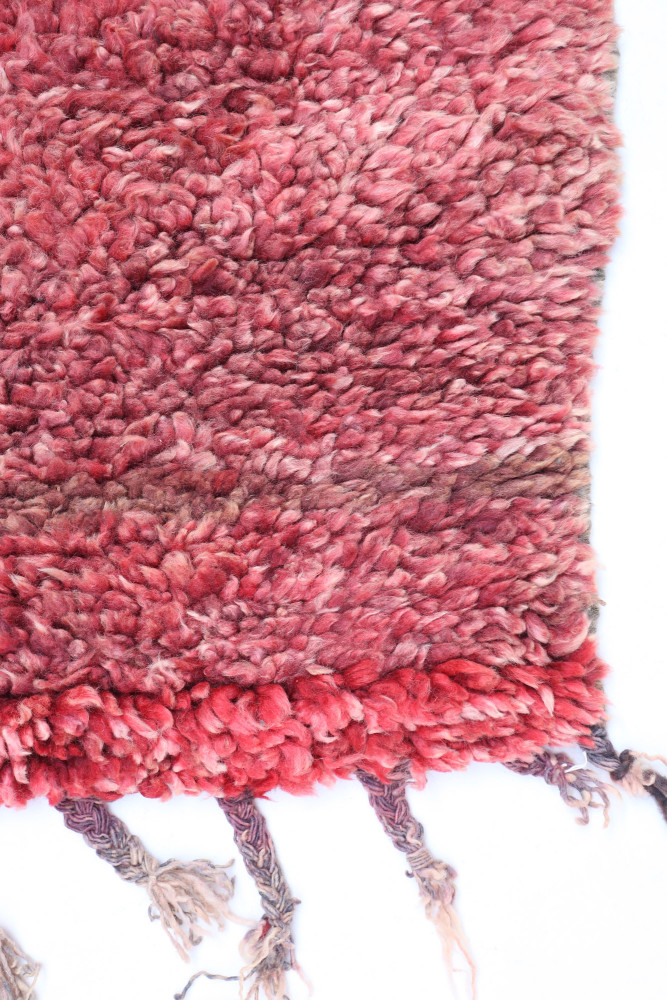 Tapis berbère en laine, aux teintes rouges et roses, avec des motifs texturés et un style traditionnel artisanal.