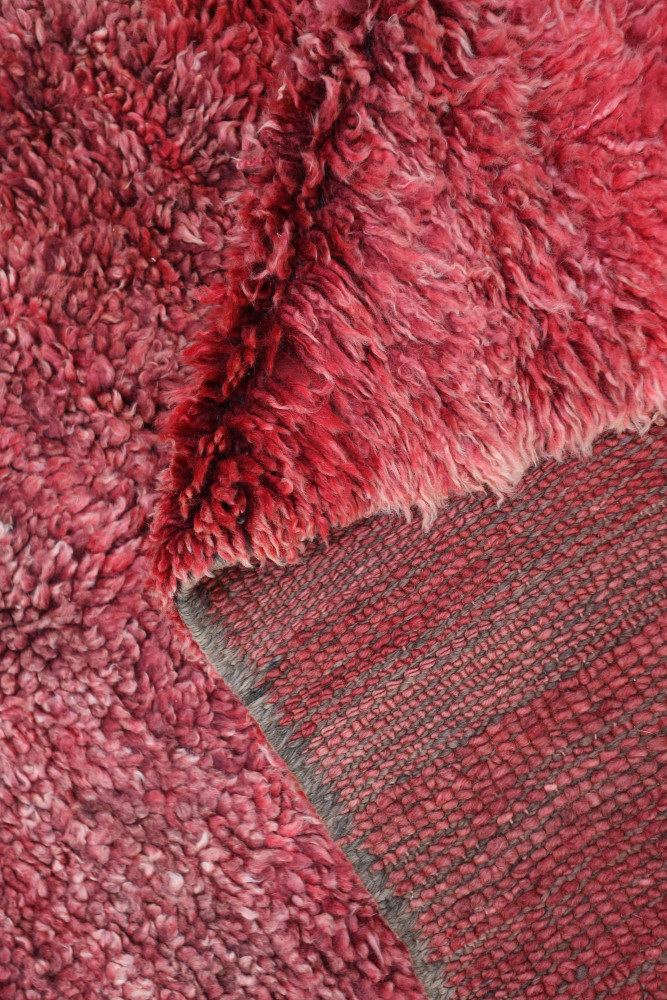 Tapis berbère en laine rouge, présentant des motifs texturés et un design authentique alliant douceur et chaleur.