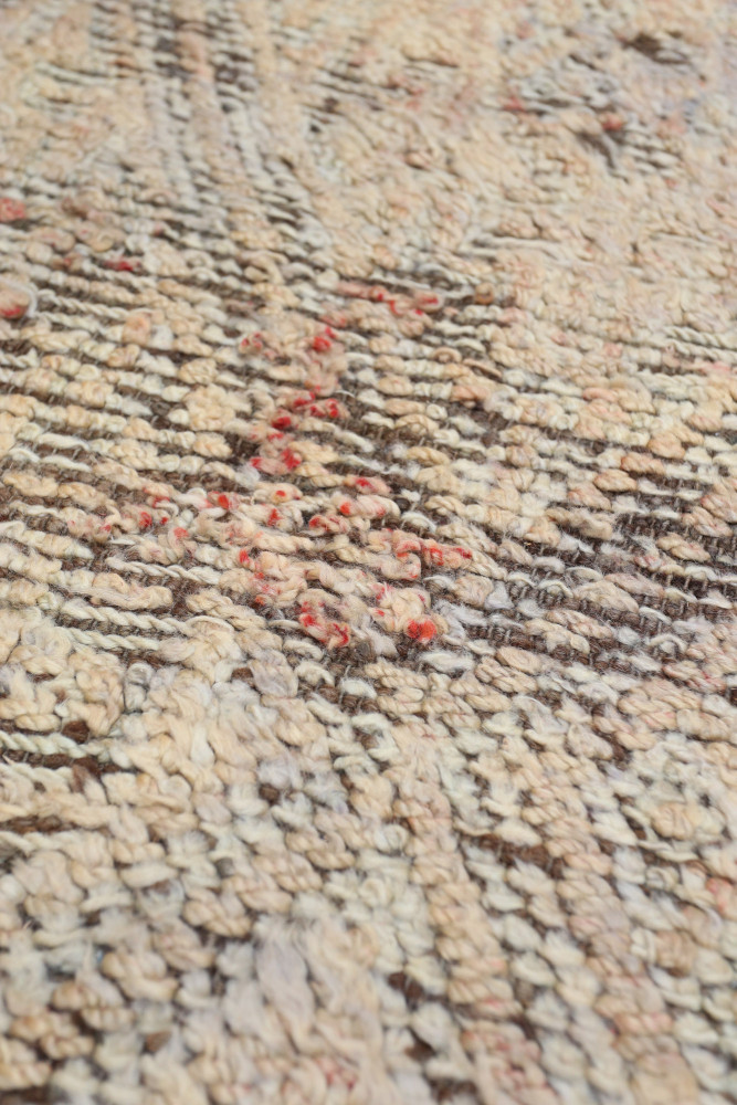 Tapis berbère aux motifs organiques, couleurs beige et marron, avec des touches de rouge sur une texture rugueuse.