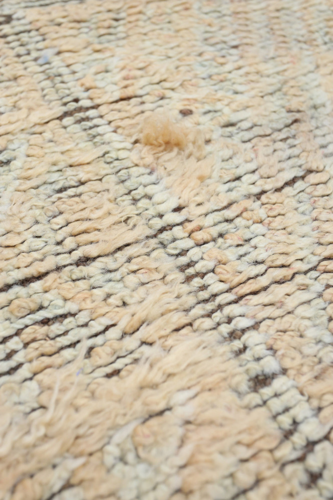 Tapis berbère en mailles douces, aux teintes beige et écru, ornés de motifs géométriques subtils.