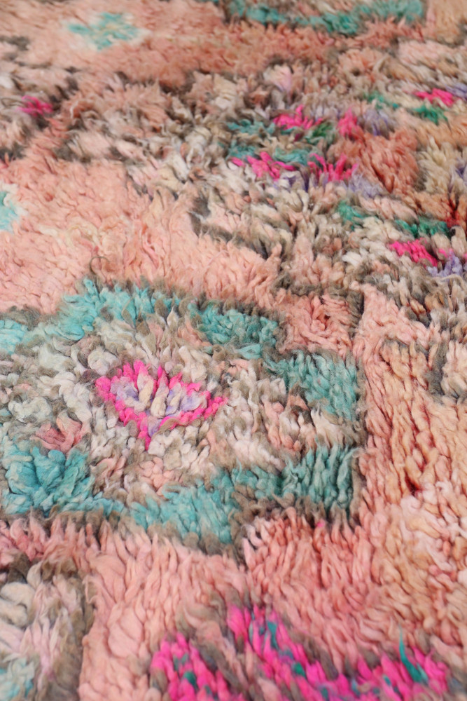 Tapis berbère aux motifs géométriques, dominé par des teintes roses, bleues et marron, apportant une touche chaleureuse.