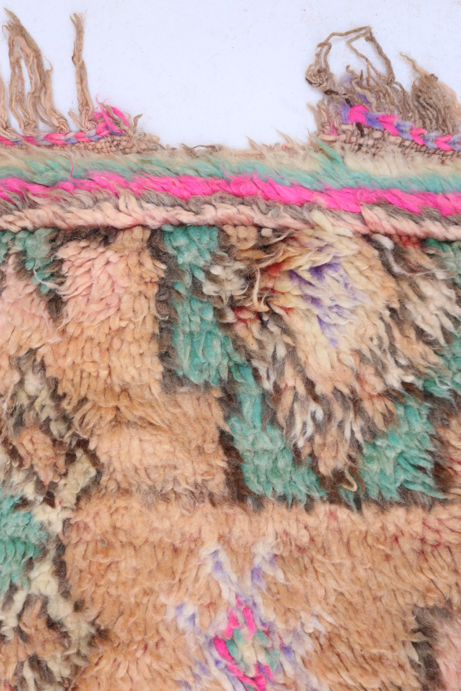 Tapis berbère aux couleurs terreuses, motifs géométriques, dominé par des teintes de rose et de vert.