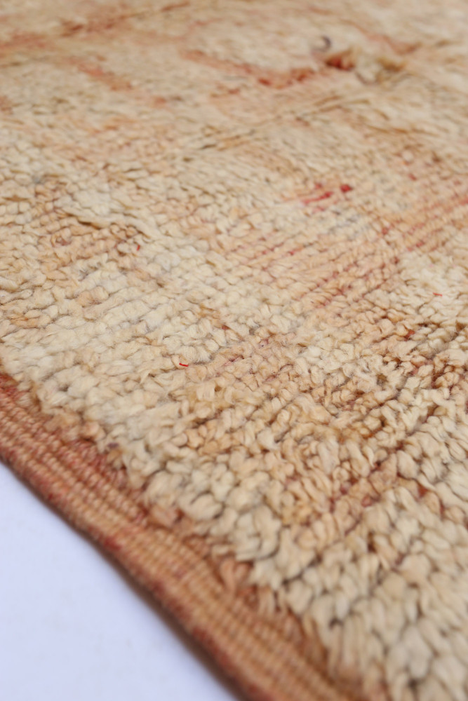 Tapis berbère en laine beige avec des motifs subtils et des nuances de rouge, offrant une texture chaleureuse et authentique.