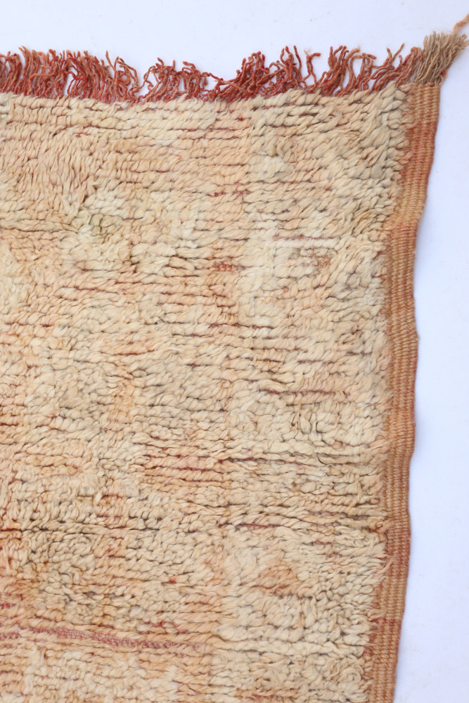 Tapis berbère aux tons crème et roux, présentant des motifs géométriques et une texture tissée à la main.