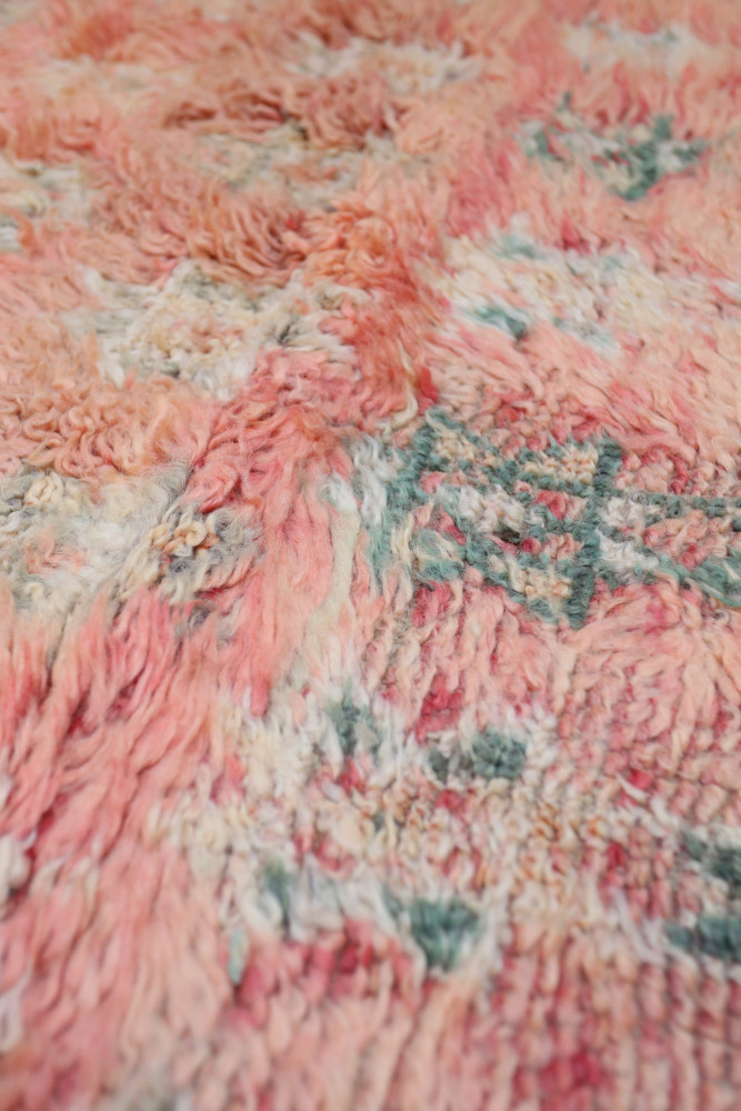 Tapis berbère aux teintes douces de rose et vert, orné de motifs géométriques subtils et texture laineuse.