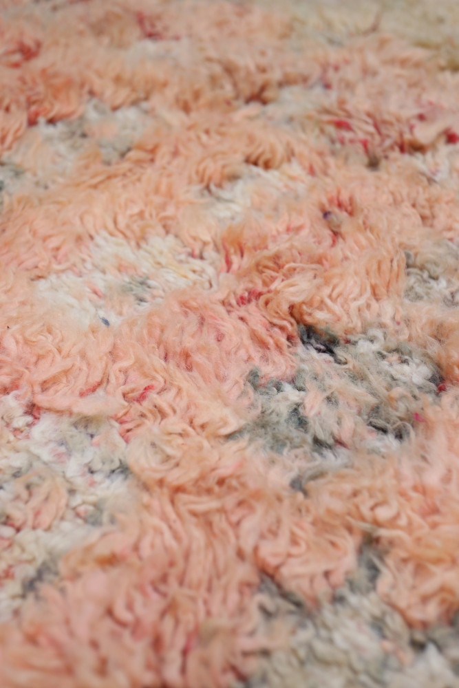 Tapis berbère aux teintes roses et grises avec des motifs texturés et une finition douce et luxueuse.