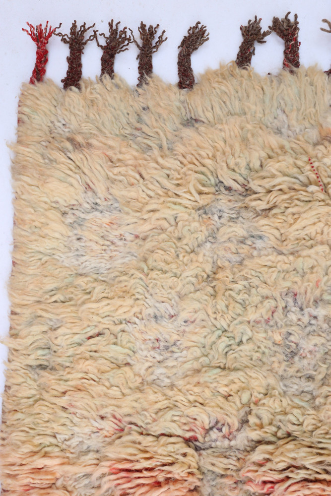 Tapis berbère artisanal avec des motifs texturés en beige, crème et touches de rouge, idéal pour une décoration chaleureuse.