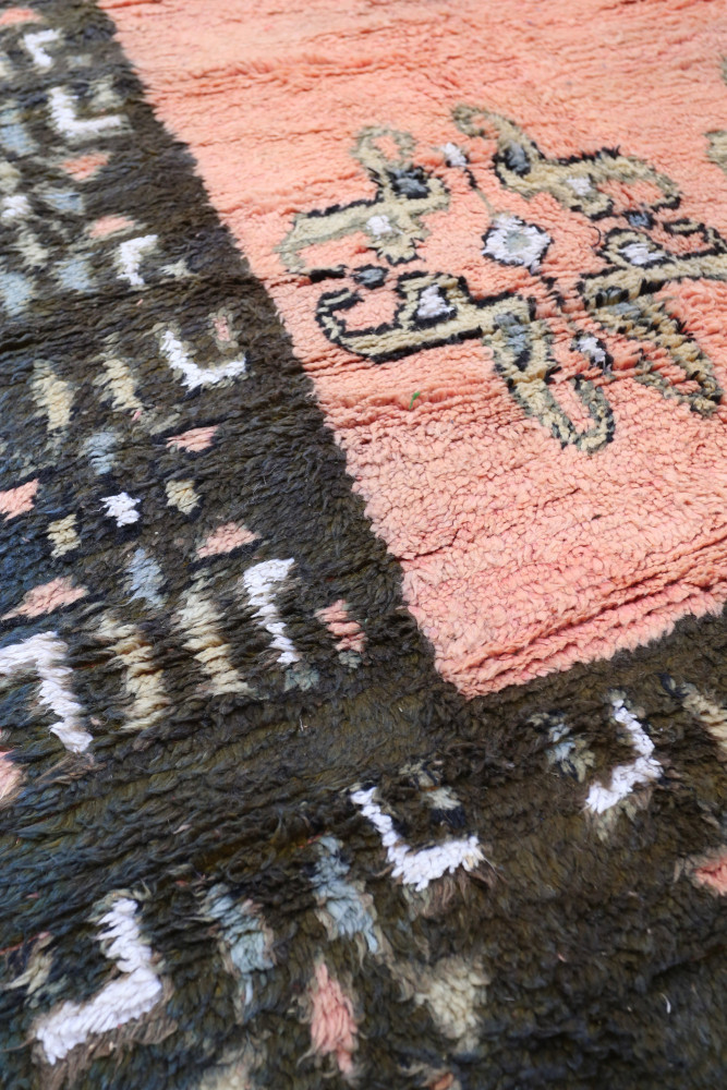 Tapis berbère aux motifs géométriques, dominé par des teintes roses et noires, ajoutant une touche artisanale élégante.
