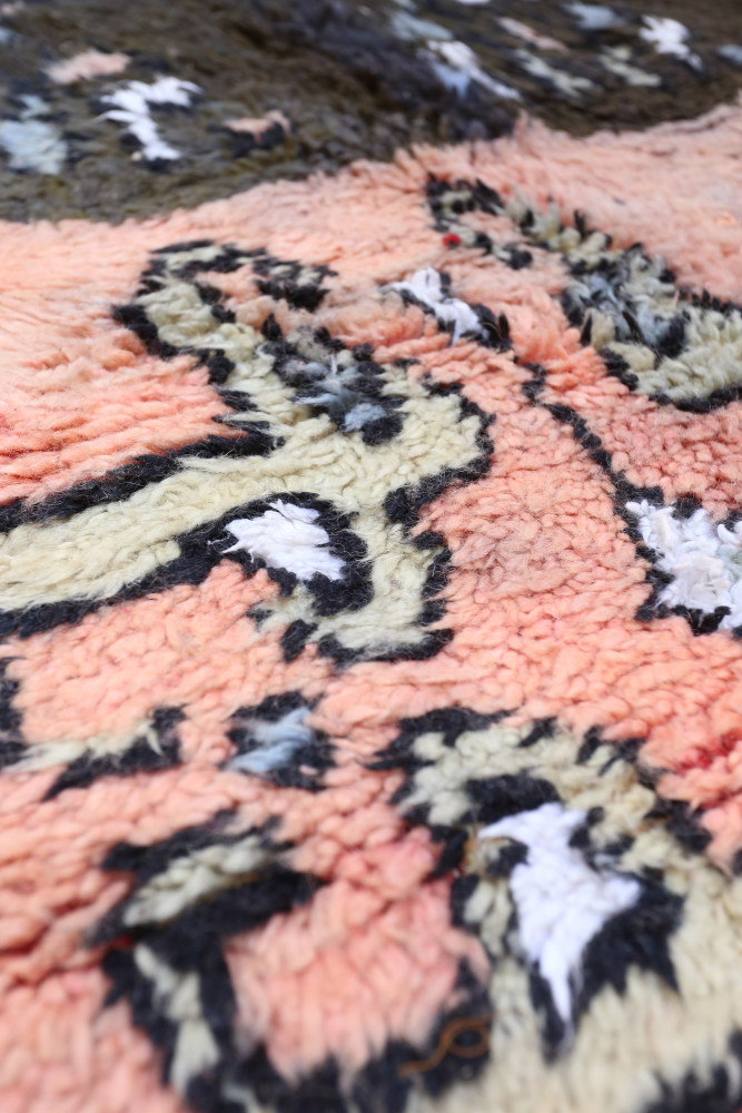 Tapis berbère aux motifs géométriques, couleurs roses, noirs et blancs, apportant une touche artisanale et chaleureuse.
