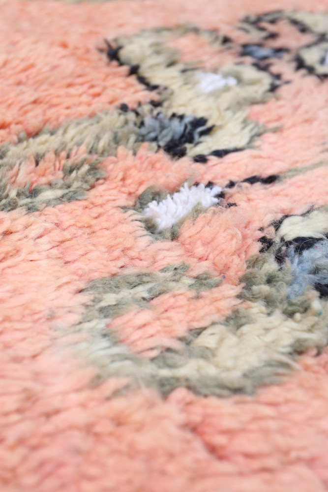 Tapis berbère aux tons rose pâle et beige, orné de motifs abstraits et texturés.
