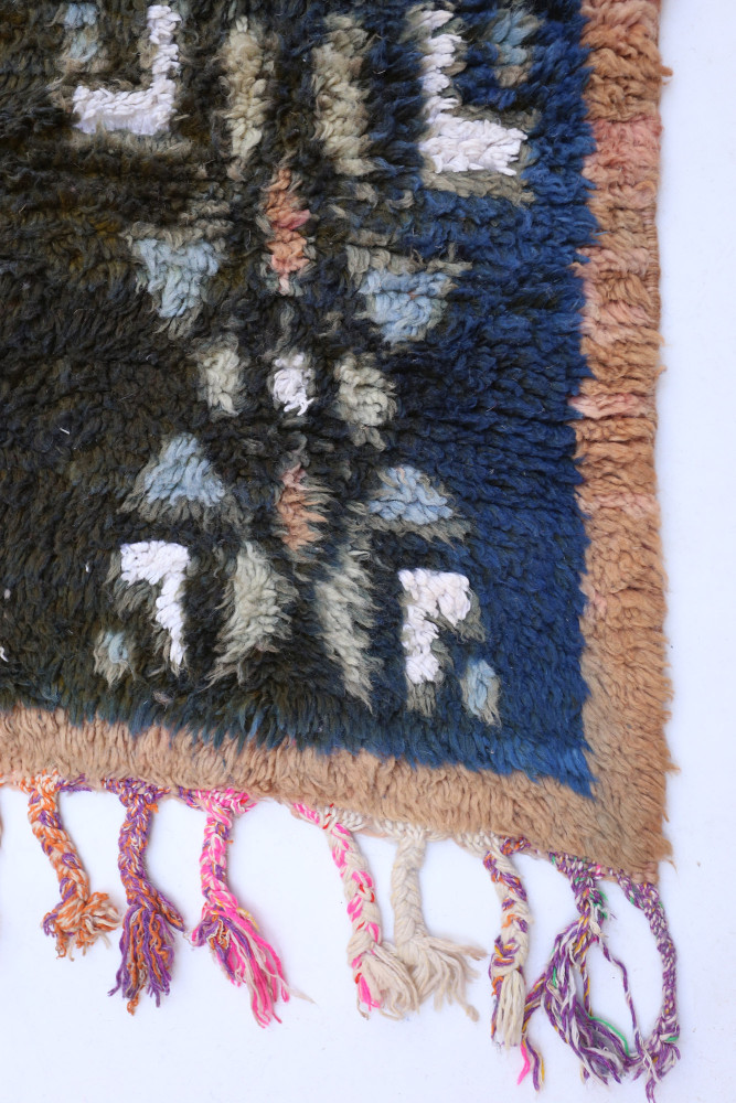 Tapis berbère aux motifs géométriques avec des couleurs bleu, crème et beige, bordé de franges colorées.