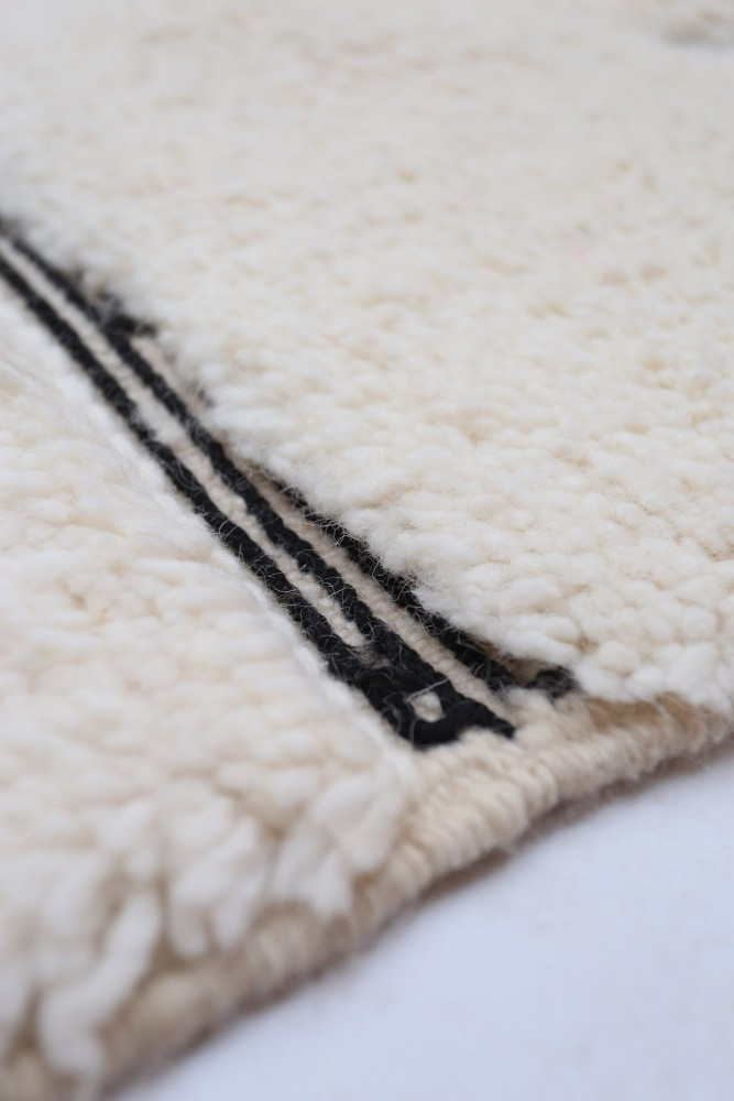 Tapis berbère en laine crémeux orné de motifs noirs géométriques et de lignes épurées.