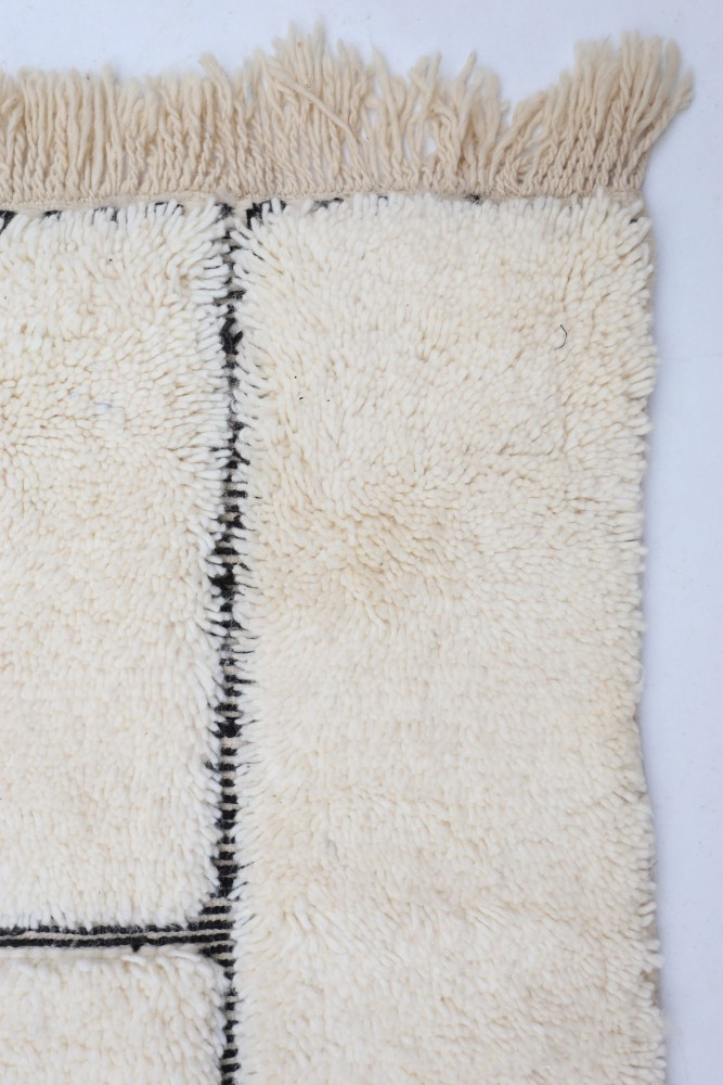 Tapis berbère en laine de couleur crème avec des motifs géométriques noirs élégants et des franges douces.