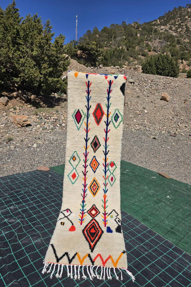 Tapis berbère en coton crème décoré de motifs géométriques colorés dans des teintes vives de rouge, bleu et orange.
