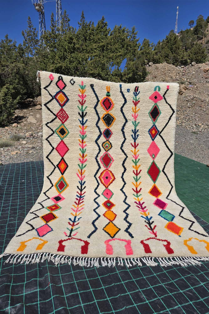 Tapis berbère aux motifs géométriques colorés dans des nuances de rose, orange, bleu et blanc créant une ambiance chaleureuse.