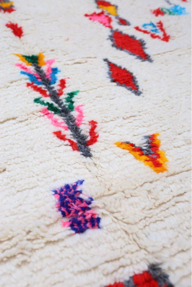 Tapis berbère avec un fond crème orné de motifs colorés en rouge, bleu, vert et rose.