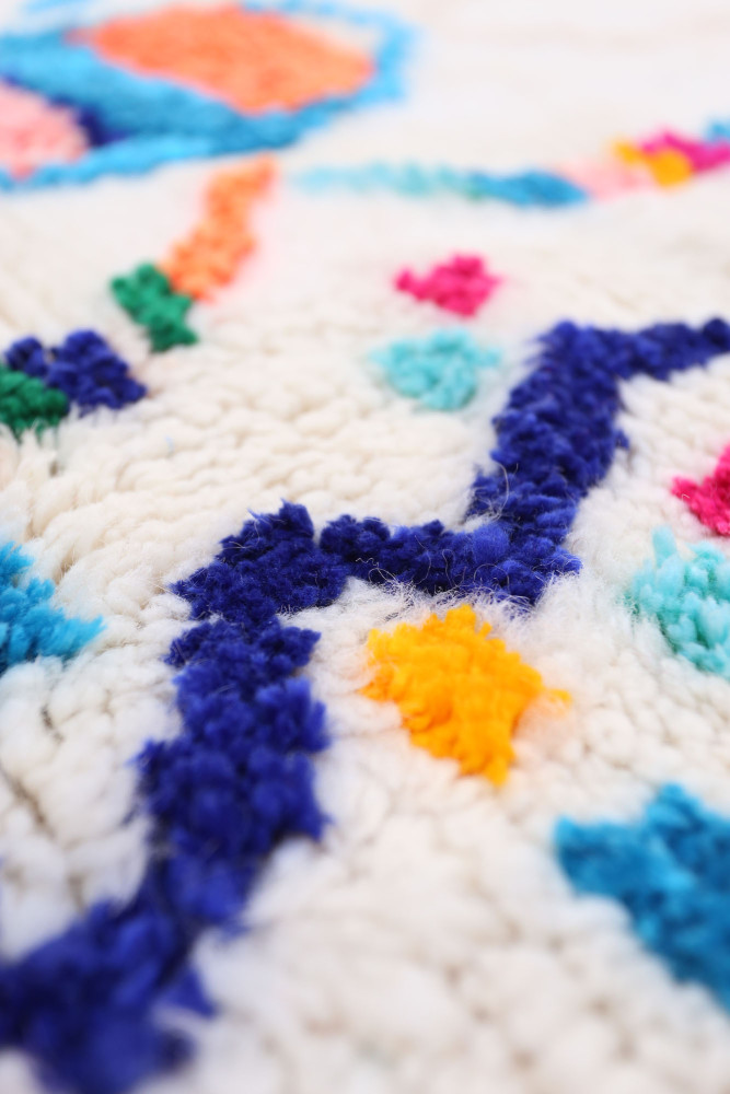 Tapis berbère coloré avec des motifs géométriques en bleu, rose et orange sur fond blanc.