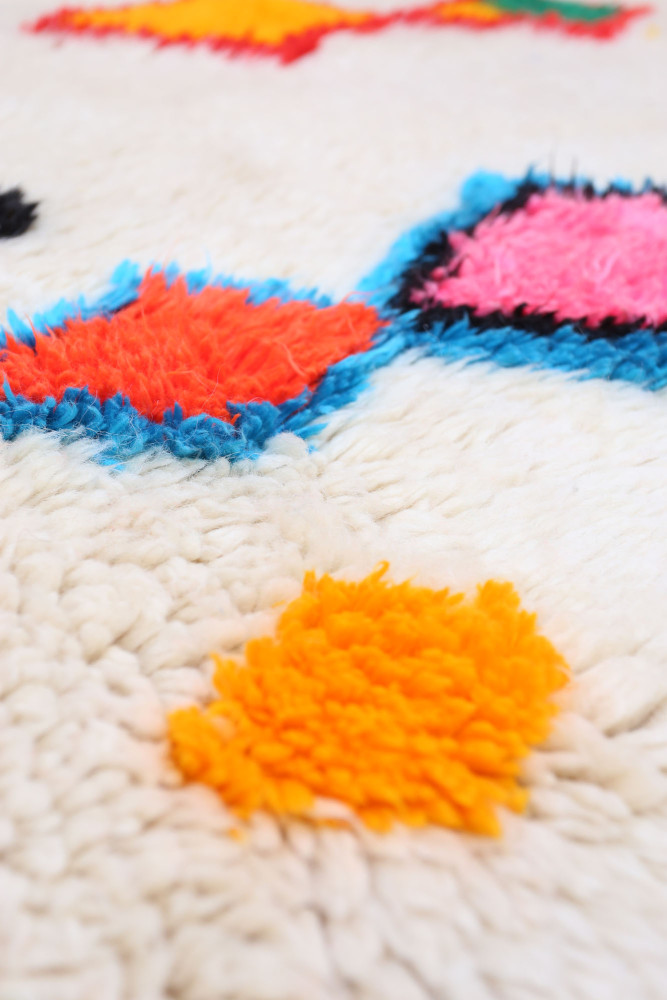 Tapis berbère aux motifs colorés avec des formes géométriques en rose, orange, bleu sur un fond crémeux.