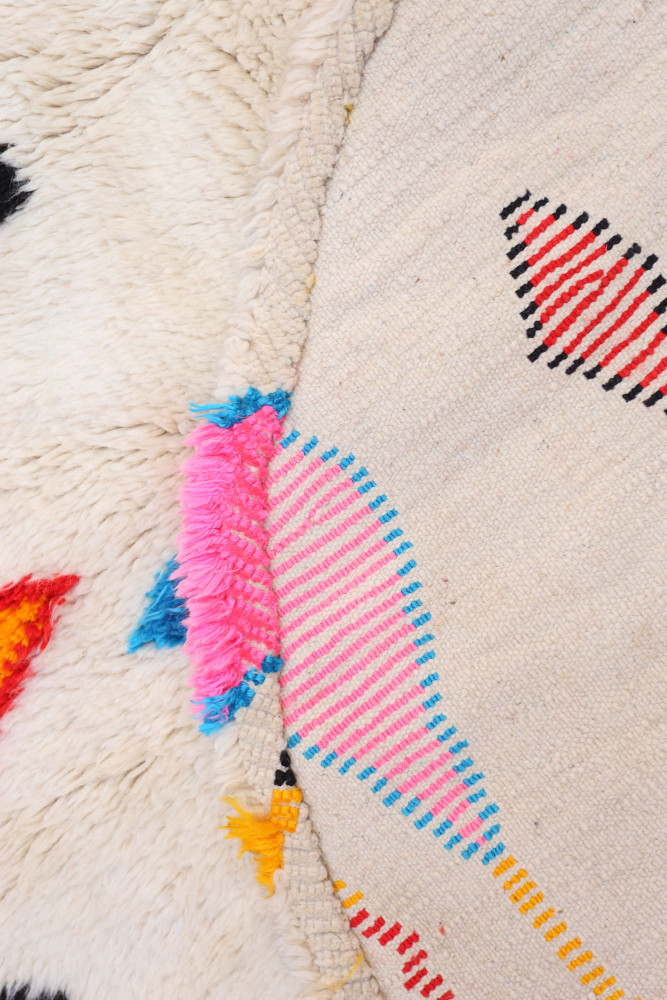 Tapis berbère aux motifs colorés, dominé par des teintes crème, rose, bleu et orange, avec des franges décoratives.