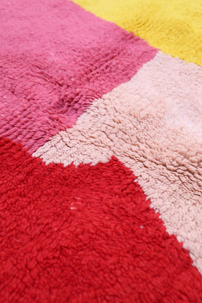 Tapis berbère coloré avec des motifs géométriques en rouge, rose, jaune et beige, offrant une texture douce et moderne.