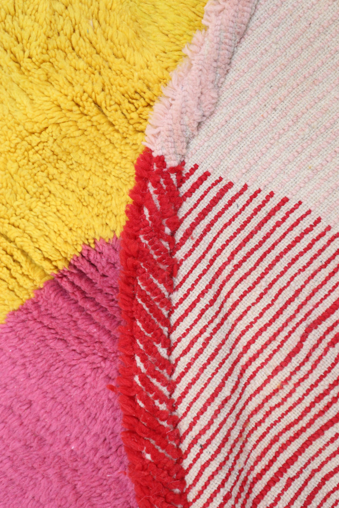 Tapis berbère aux couleurs vives, mélanges de rose, jaune et rouge avec des motifs géométriques et des franges.