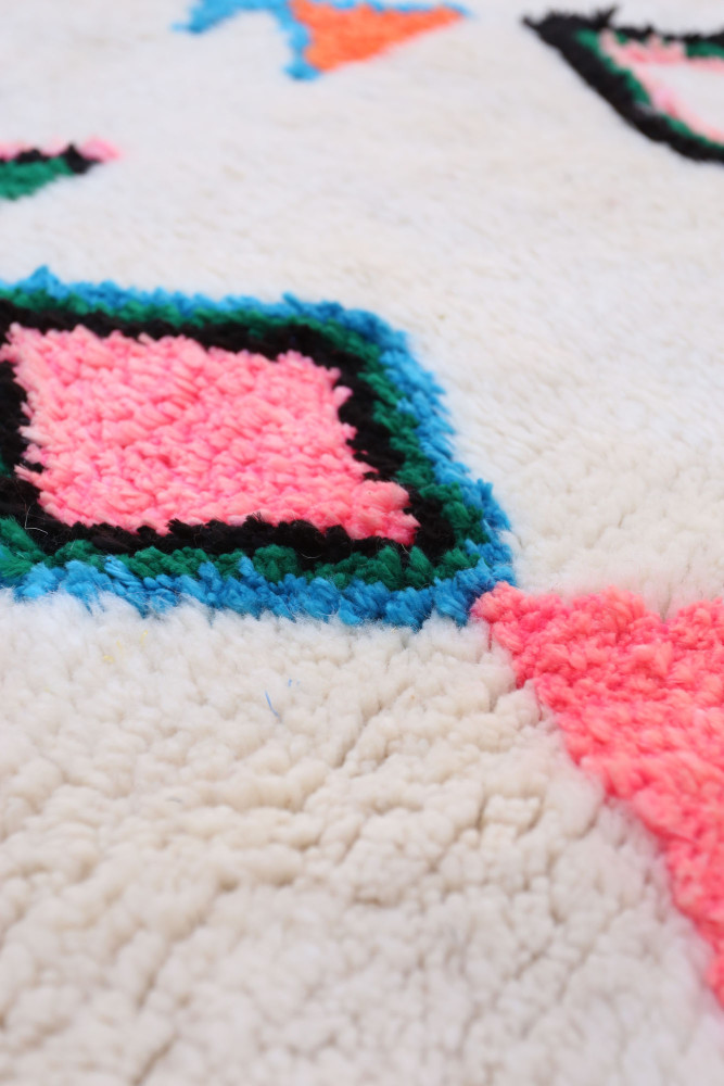 Tapis berbère géométrique en blanc avec motifs colorés en rose, vert et bleu.