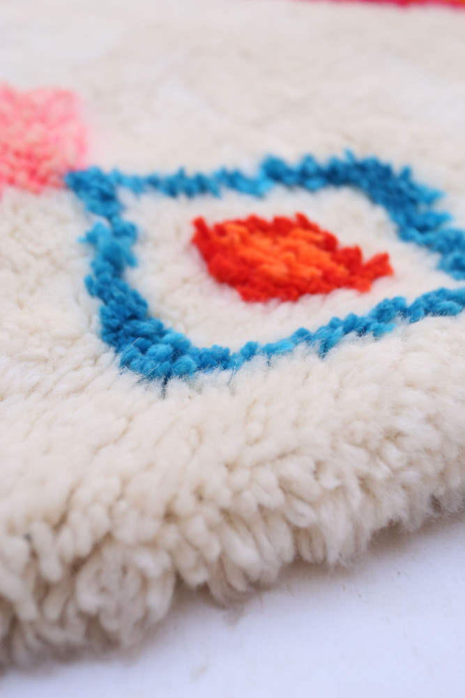 Tapis berbère en laine crème avec motifs géométriques colorés en bleu et orange.