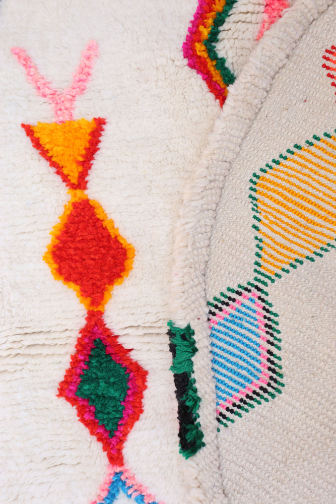 Tapis berbère aux motifs géométriques colorés avec des tons vifs de rouge, vert, orange et rose sur fond crème.