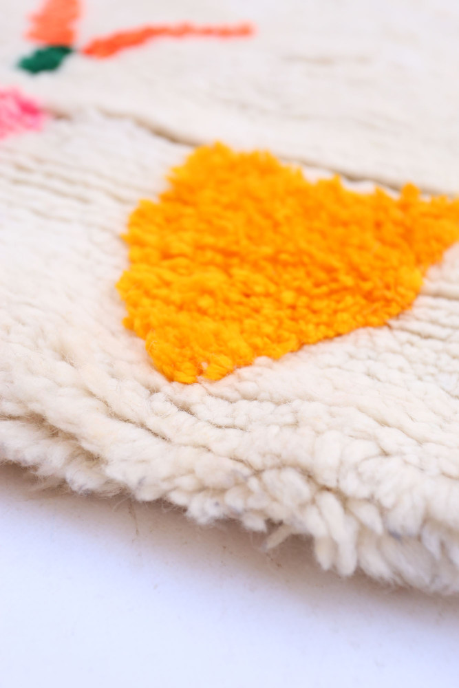 Tapis berbère en laine, avec des couleurs vives comme le jaune et le rose, ornés de motifs géométriques.