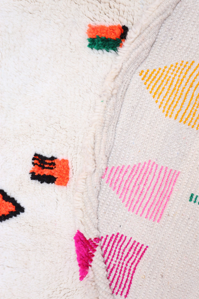 Tapis berbère élégamment texturé, avec des motifs colorés en rose, orange, vert et jaune sur fond blanc.