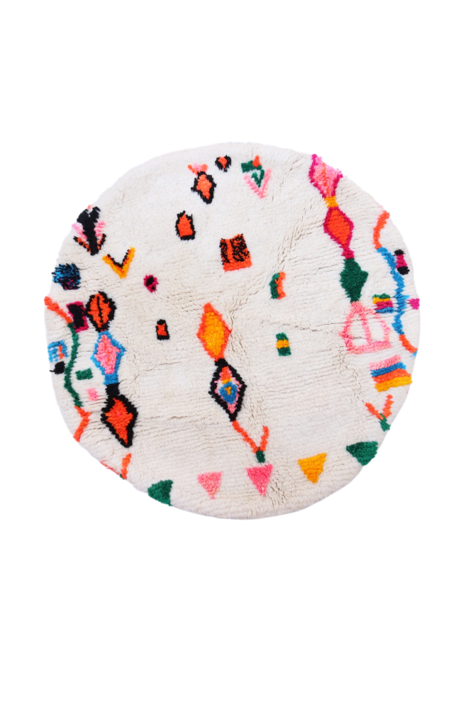 Tapis berbère rond aux motifs colorés, dominé par le blanc, le rose et le vert, parfait pour un intérieur moderne.