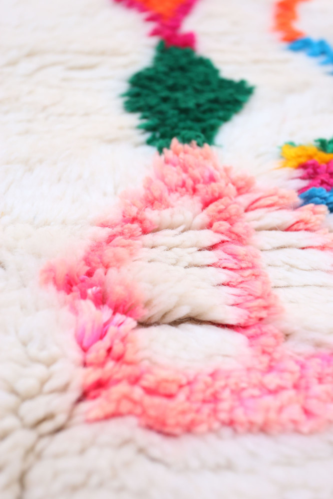 Tapis berbère couleur crème avec des motifs géométriques en rose, vert et bleu, apportant une touche moderne et colorée.