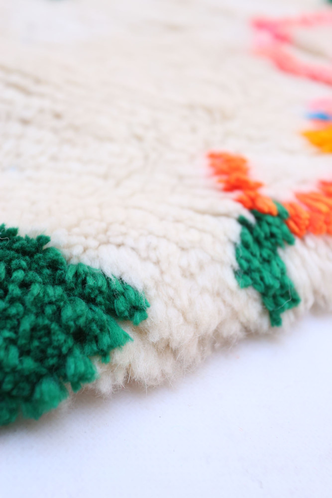 Tapis berbère à motifs colorés sur fond crème avec des touches de vert et orange, ajoutant une ambiance chaleureuse.