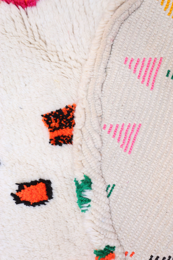 Tapis berbère en laine claire avec des motifs géométriques colorés, dont du rose, orange et vert.
