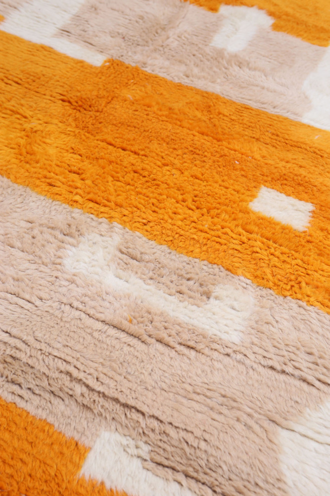 Tapis berbère aux couleurs orange et beige, avec des motifs géométriques et texture douce.