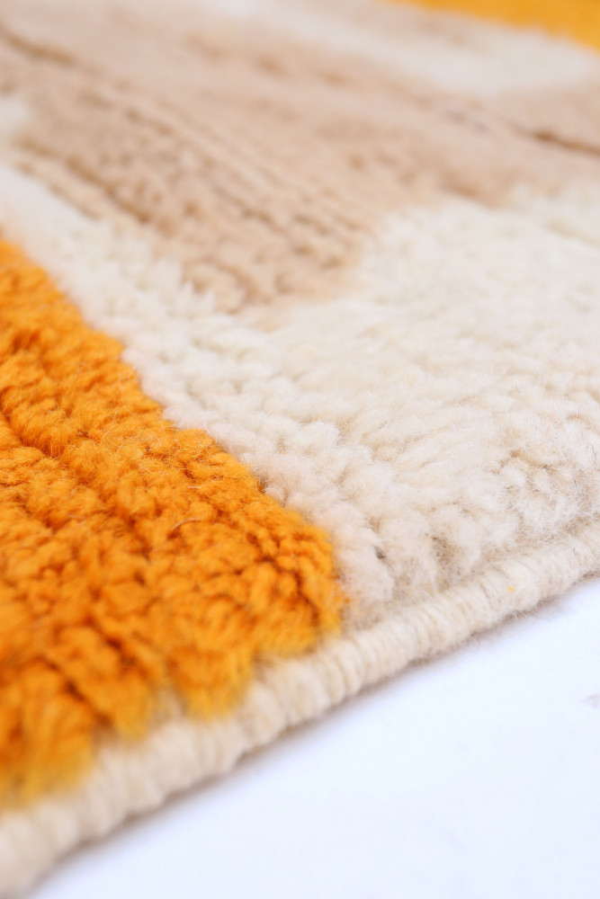 Tapis berbère aux couleurs orange, beige et crème avec des motifs géométriques et texturés.