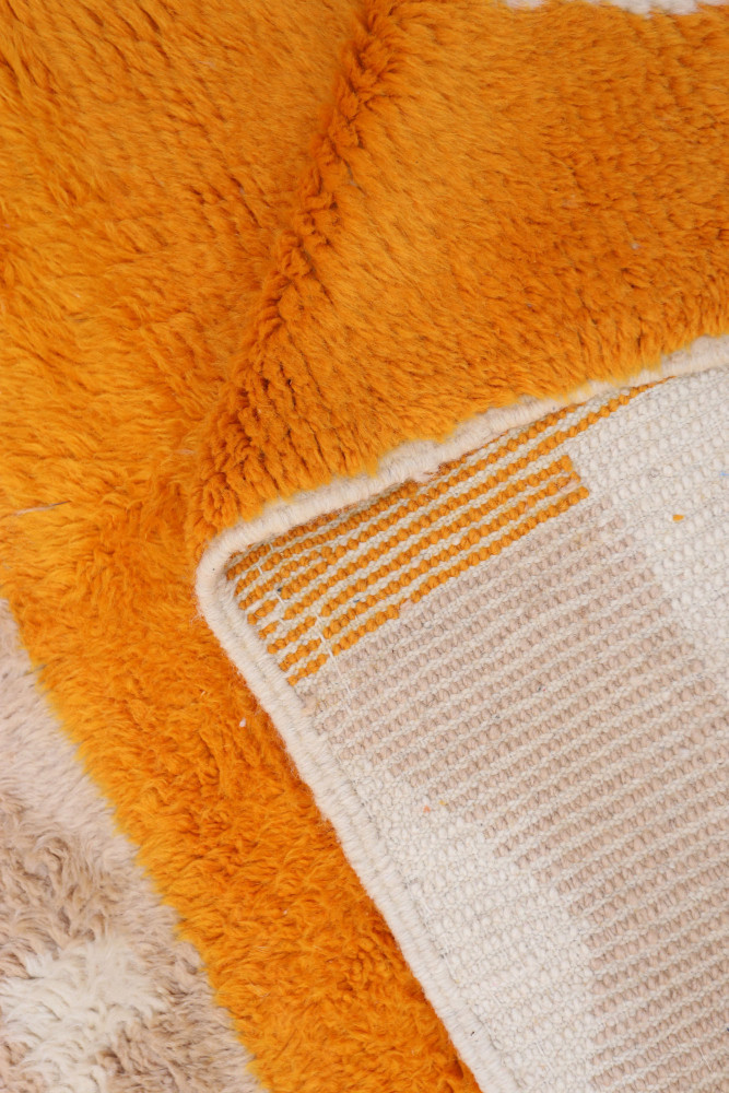 Tapis berbère aux motifs géométriques, dominé par des tons orange et crème, offrant une texture douce et chaleureuse.