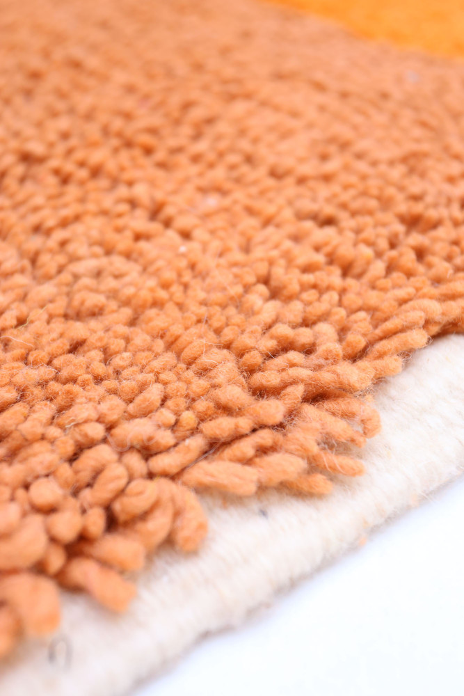 Tapis berbère en laine doux, avec des teintes orange et des motifs texturés, idéal pour un décor chaleureux et moderne.