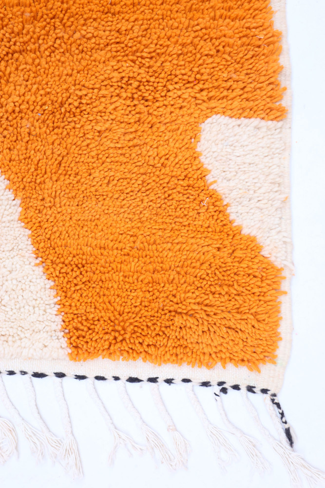 Tapis berbère en laine aux motifs géométriques avec des couleurs orange et crème, idéal pour embellir votre intérieur.