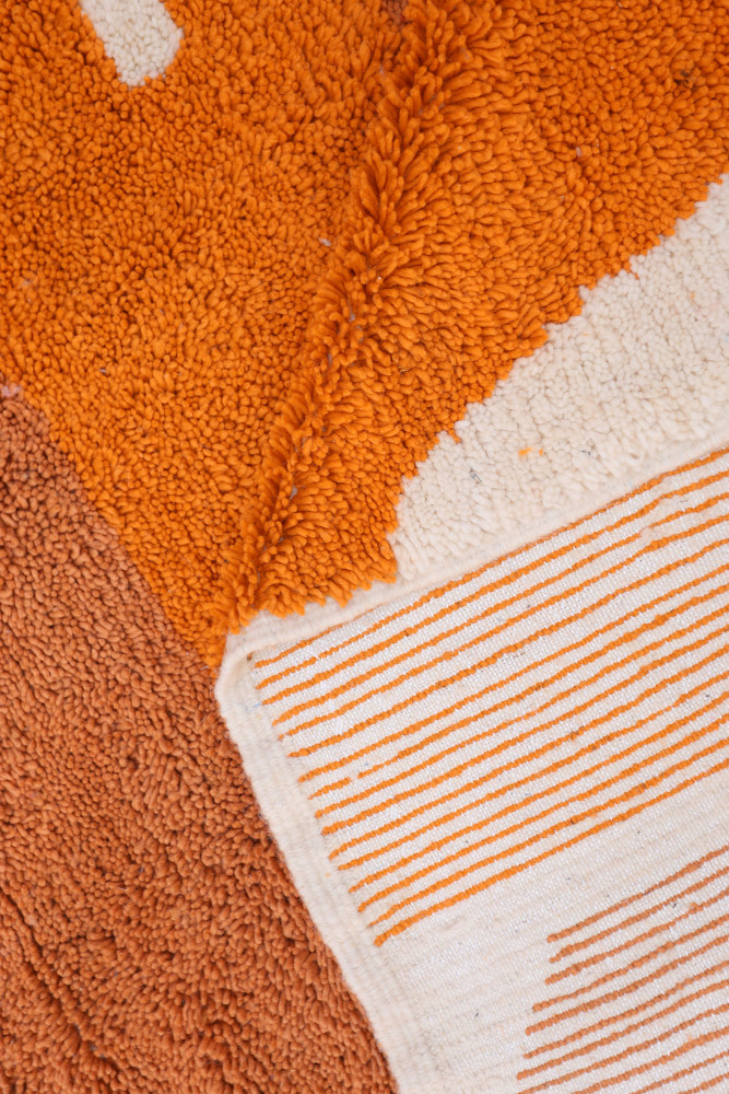 Tapis berbère aux motifs géométriques avec des couleurs orange, beige et des rayures stylisées.