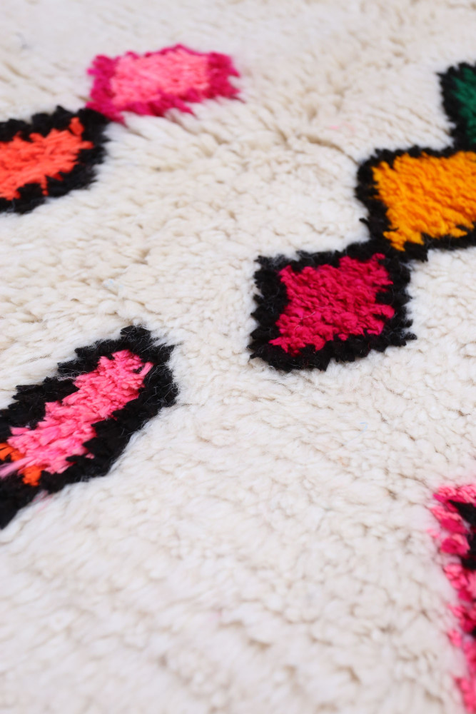 Tapis berbère au fond crème agrémenté de motifs géométriques colorés en rose, noir et vert.