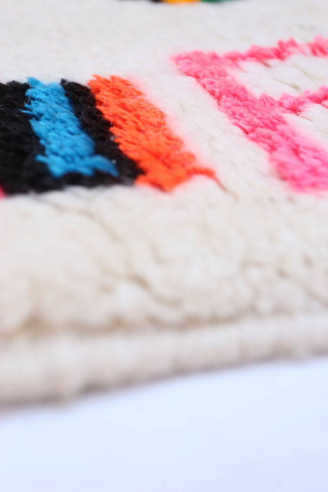 Tapis berbère contemporain aux teintes vives de bleu, noir, rose et orange, orné de motifs géométriques.