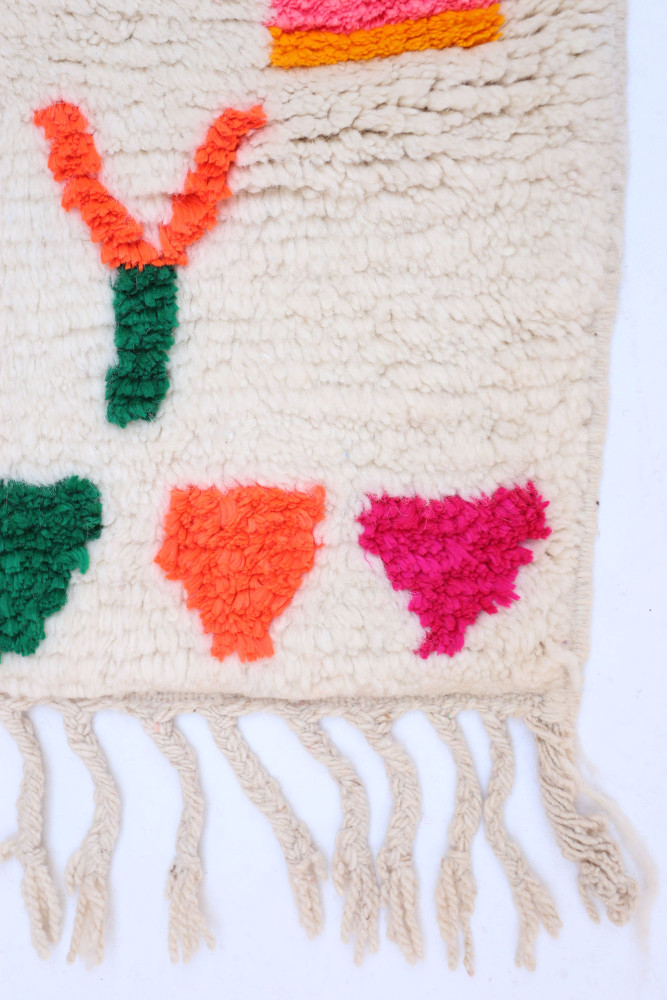 Tapis berbère aux motifs géométriques colorés dans des teintes de rose, vert, orange sur fond crème.