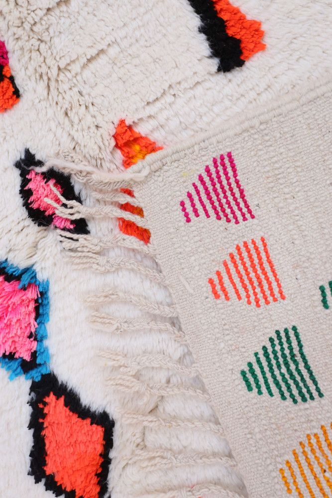 Tapis berbère aux motifs colorés en rose, noir, orange et vert, ajoutant une touche moderne à votre intérieur.