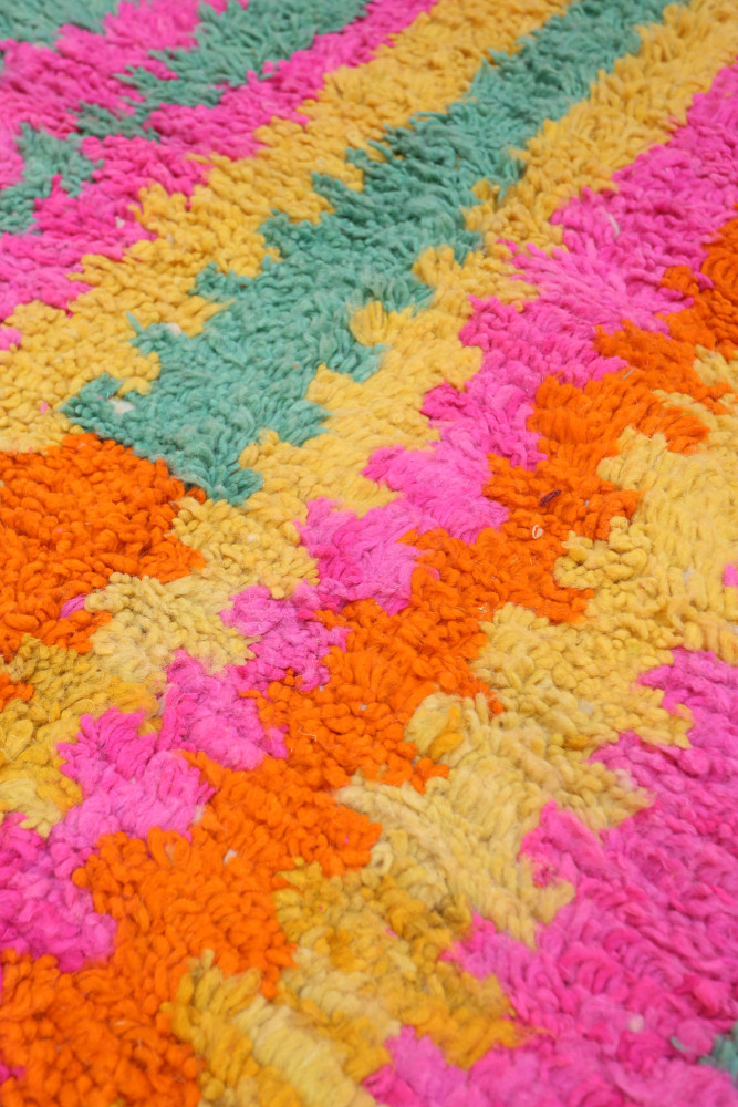 Tapis berbère coloré avec des motifs géométriques en rose, orange, jaune et vert.