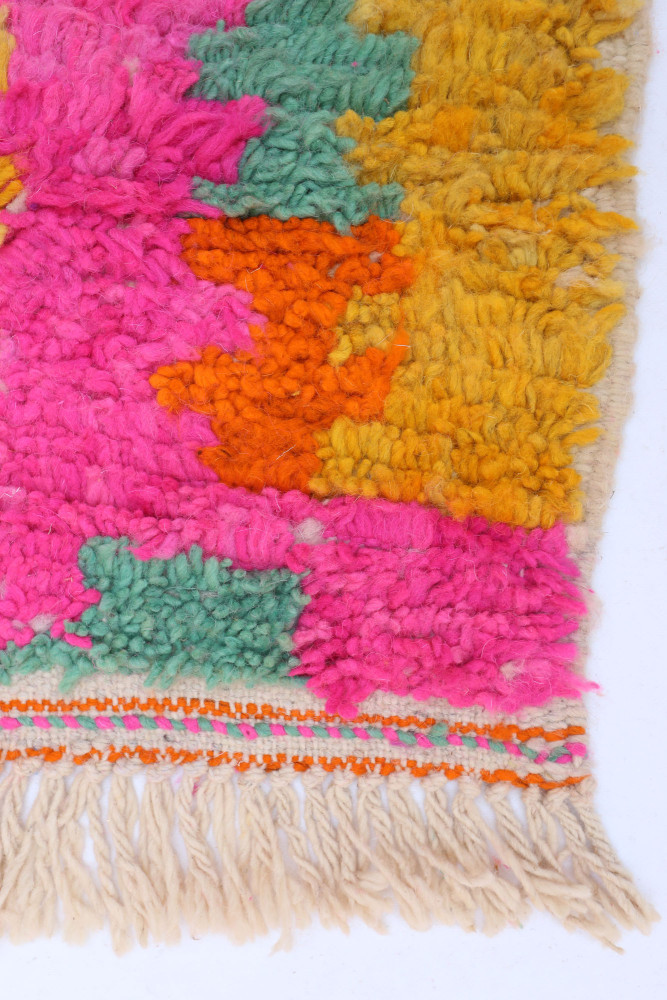 Tapis berbère aux couleurs vives de rose, orange, jaune et vert, avec des motifs texturés et une finition à franges.